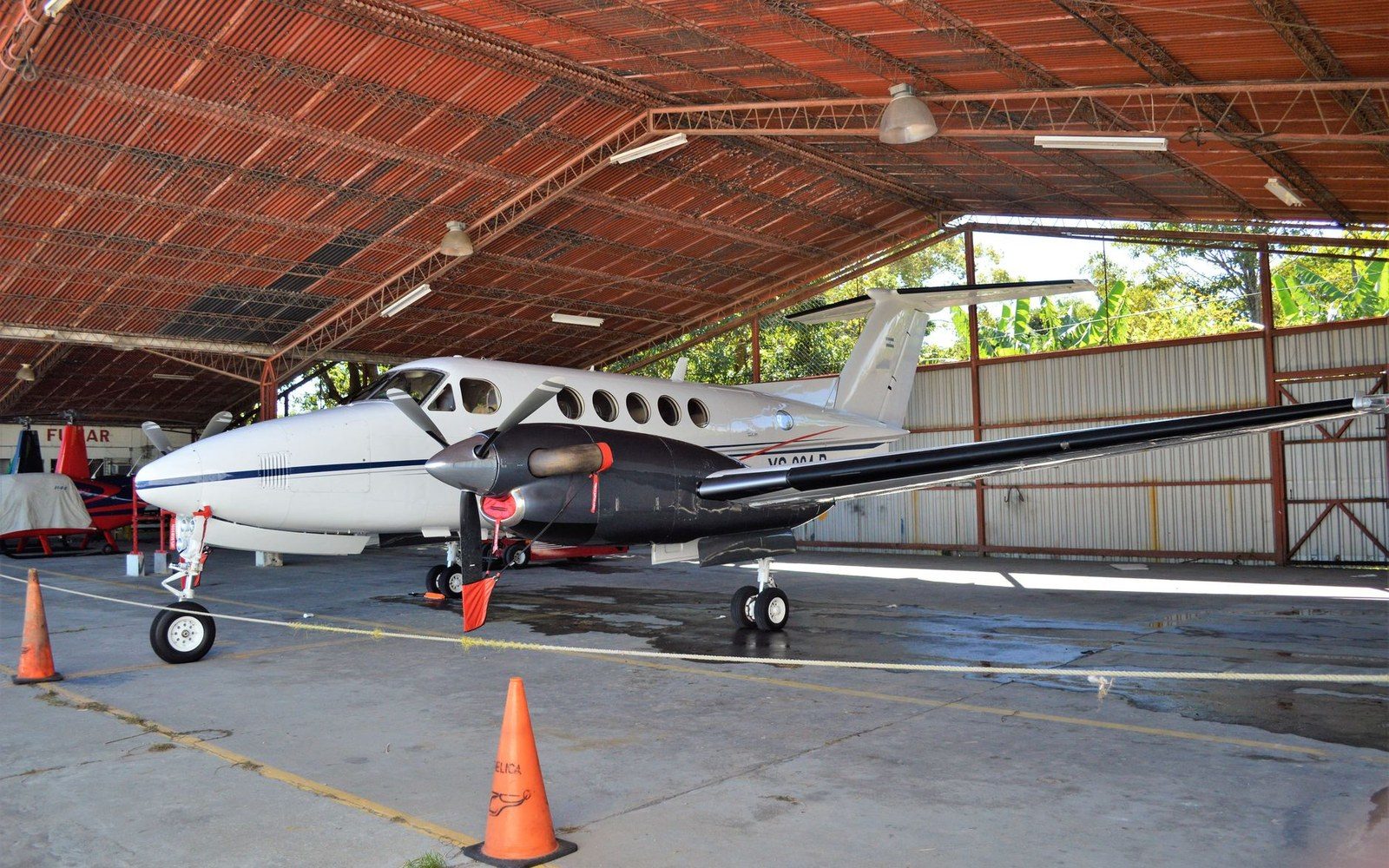 Twin-engine turboprop plane parked under a rusted metal hangar roof