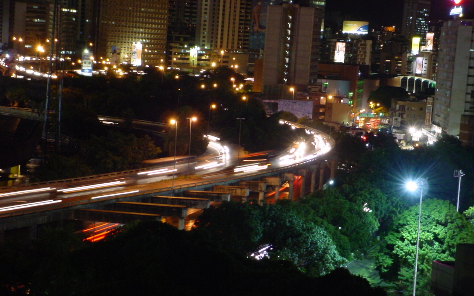 Long-exposure night view of an elevated highway curving through a lit-up city skyline