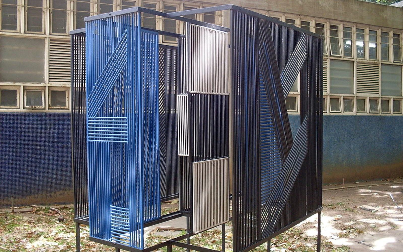 Blue and metallic vertical rods form a walk-through kinetic sculpture outside a tiled building