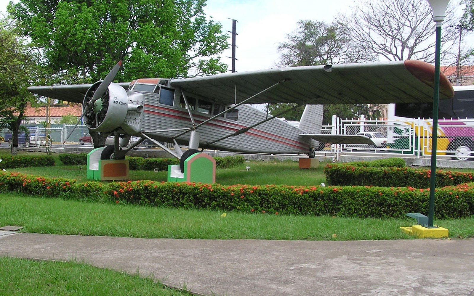 Vintage single-engine monoplane displayed on pedestals in a park with hedges