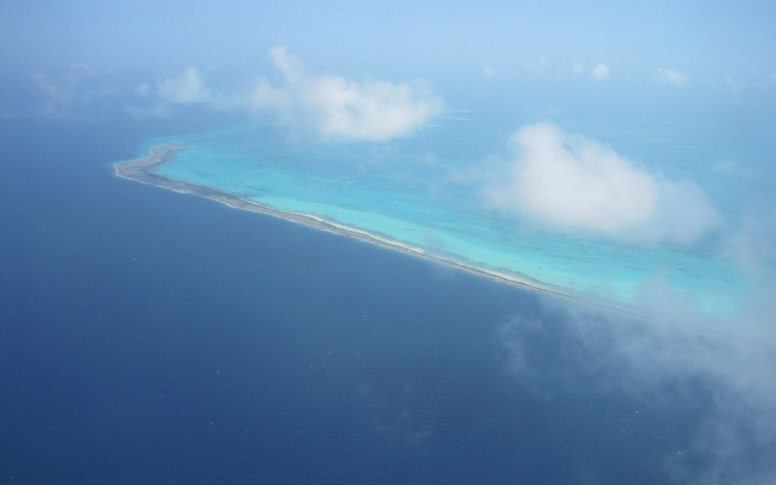 Aerial view of a coral atoll's turquoise lagoon fringed by a reef against deep blue ocean