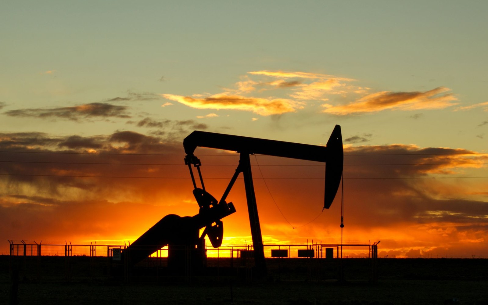 Silhouette of an oil pumpjack against a glowing orange sunset sky