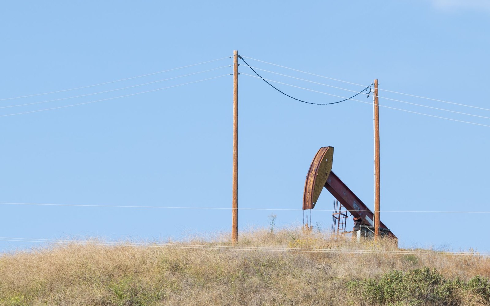 An oil pumpjack stands idle on a grassy hillside beneath power lines