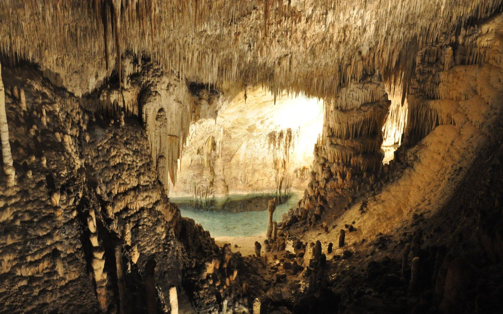 Stalactites and stalagmites surround a still turquoise pool inside a limestone cave