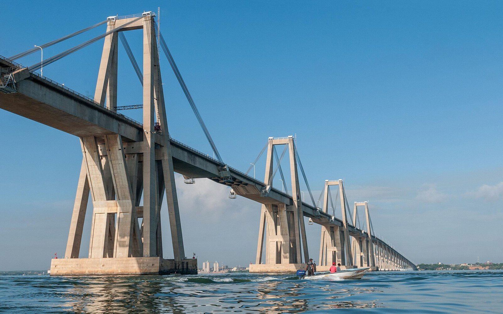 Concrete cable-stayed bridge with multiple towers spans a wide lake as a small boat passes below